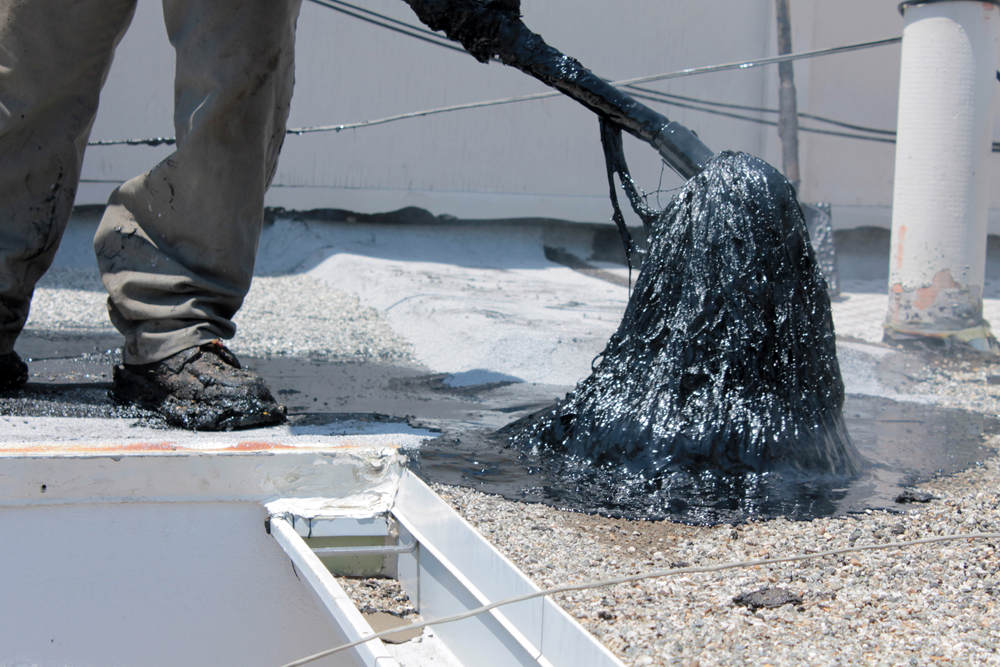 Worker applying Hot Tar aka Hot Mop to lay down Molten Tar on flat roof (Hot Mop Roofs Vs. Torch Down Roofs)